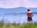 Young boy in blue swimming shorts stay in cold water of lake