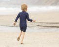 Preschool aged boy in a blue swimming suit running along a sandy shoreline Royalty Free Stock Photo