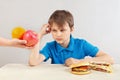 Young boy in blue at the table chooses between fastfood and fruits