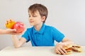 Young boy in blue at the table chooses between fastfood and healthy diet on white background Royalty Free Stock Photo