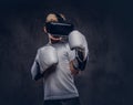 Schoolboy boxer with blonde hair dressed in a white t-shirt wearing visual reality glasses and boxing gloves, workout in Royalty Free Stock Photo