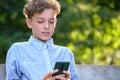 Young boy browsing his smartphone outdoors in summer park. Using cellphone for leasure and education concept