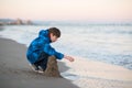 Young boy builds sand castle at the winter beach. Cute 11 years old boy at seaside, evening time.
