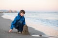 Young boy builds sand castle at the winter beach. Cute 11 years old boy at seaside, evening time. Royalty Free Stock Photo