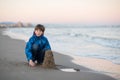 Young boy builds sand castle at the winter beach. Cute 11 years old boy at seaside, evening time. Royalty Free Stock Photo