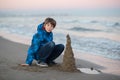 Young boy builds sand castle at the winter sea beach. Handsome teen boy playing at the seaside Royalty Free Stock Photo