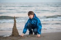 Young boy builds sand castle at the winter sea beach. Handsome teen boy playing at the seaside Royalty Free Stock Photo