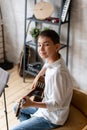 Young boy in casual clothing sits on chair with acoustic guitar in hands and posing