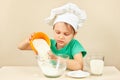 Young boy in chefs hat pours flour for baking cake