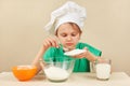 Young boy in chefs hat pours sugar for baking cake