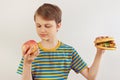 Young boy chooses between fastfood and fruit on white background Royalty Free Stock Photo