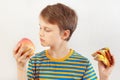 Young boy chooses between sandwich and apple on white background Royalty Free Stock Photo