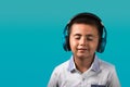 Young boy with closed eyes and smiling, happy wearing headphones listening to music close up portrait with blue background Royalty Free Stock Photo