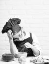 Young boy cute cook chef in red uniform and hat on stained face with glasses sitting on table with colorful bowls, tasty