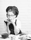 Young boy cute cook chef in red uniform and hat on stained face with glasses sitting on table with colorful bowls, tasty