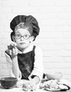 Young boy cute cook chef in red uniform and hat on stained face with glasses sitting on table with colorful bowls, tasty