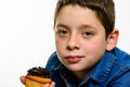 Young boy with denim shirt eating chocolate cupcake, on white isolated background. Close up.