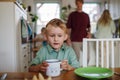 Young boy drinking cup of warm milk, cocoa in the morning. Family eating breakfast together in home kitchen. Healthy Royalty Free Stock Photo