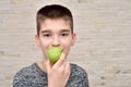 Young boy eating green apple in front of the brick wall