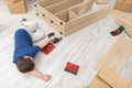 A young boy falls asleep on the floor while assembling furniture.