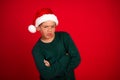 Grumpy boy wearing a Santa hat standing against a bright red background feeling unsatisfied during the Christmas season Royalty Free Stock Photo