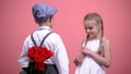 Young boy in formal clothes hiding roses behind back and presenting to girl