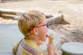 Young boy with glasess sits outside at table and eats ice cream