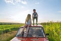 Young boy in grey t-shirt standing on the roof of the red retro car and looking scary at the left side her sister in Royalty Free Stock Photo