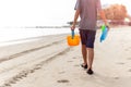 Young boy hand carrying plastic toys walking along the beach.