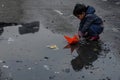 A young boy happily playing with a small paper boat as it floats in a puddle, A child making paper boats to float on water-filled Royalty Free Stock Photo