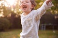 Young Boy Having Fun In Garden Chasing And Bursting Bubbles