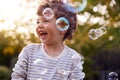 Young Boy Having Fun In Garden Chasing And Bursting Bubbles