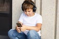 Young boy in headphones with smartphone listens to music in summer park Royalty Free Stock Photo