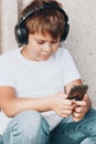 young boy in headphones with smartphone listens to music in summer park Royalty Free Stock Photo