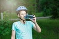 Young boy in helmet and green t shirt cyclist drinks water from bottle in the park. Smiling cute Boy on bicycle in the forest Royalty Free Stock Photo