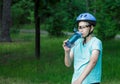 Young boy in helmet and green t shirt cyclist drinks water from bottle in the park. Smiling cute Boy on bicycle in the forest