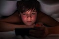 Young boy hiding under the blanket and watching his phone Royalty Free Stock Photo