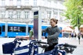 Young boy hiring bicycle with machine in city, road trafic and pedestrians in background.