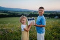 Young boy his sister holding model of house with installed solar panels.