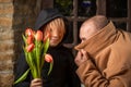 a young boy is holding a bouquet of flowers next to a man in a coat covering his face. Conspirators preparing with surprise Royalty Free Stock Photo