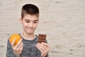 Young boy holding orange fruit and chocolate bar in front of the brick wall