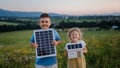 Young boy holding solar panel and his sister holding model of house with installed solar panels.