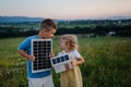 Young boy holding solar panel and his sister holding model of house with installed solar panels.
