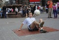 Young boy juggling with the soccer ball on the street, blurred people watching on a background