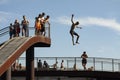 Young boy jumping from a high point with arms and legs out into the water while others are watching. Royalty Free Stock Photo