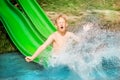 Young boy or kid has fun splashing into lake after going down water slide during summer. Vacation and childhood concept Royalty Free Stock Photo