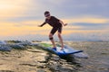 Young boy kid surfer riding waves with soft board in Rayong beach, Thailand. Rookie surfboard student playing on water in excited