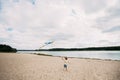 A young boy with a kite in his hands runs along the sandy beach on the banks of a picturesque river Royalty Free Stock Photo