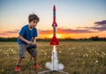 A young boy launches a small red and white model rocket using a control pad in an open field at Royalty Free Stock Photo
