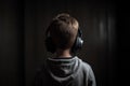 Young boy listening to music with headphones on dark background, back view, A young boy full rear view with headphone listening Royalty Free Stock Photo